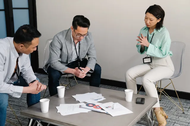 A group of colleagues in a meeting room discuss papers on a table during a business discussion. Preparing a joint campaign retrospective