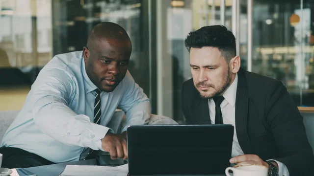 Two businessmen concentrating on a tablet, collaborating in a modern office setting. Strategic partnership marketing for B2B businesses